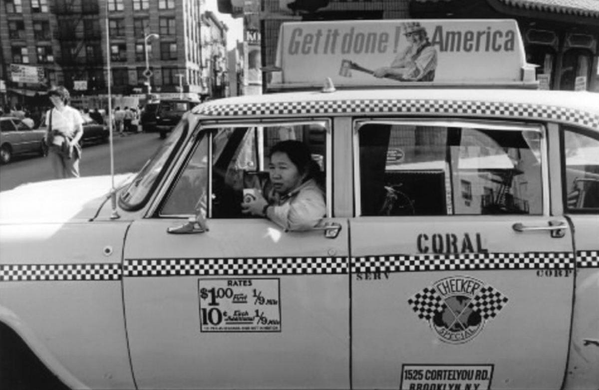 A taxi driver hangs out of the taxi window. The ad on top of the car says "Get it done America"