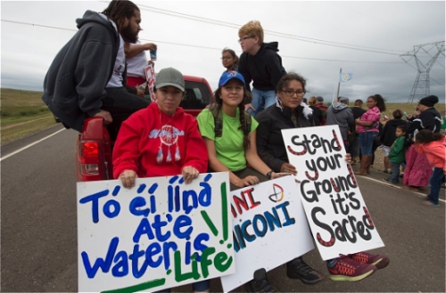 Photo by Robyn Beck. Youths hold signs in English and the Navajo language before the start of a march to a burial ground that was disturbed by the building of the Dakota Access Pipeline.