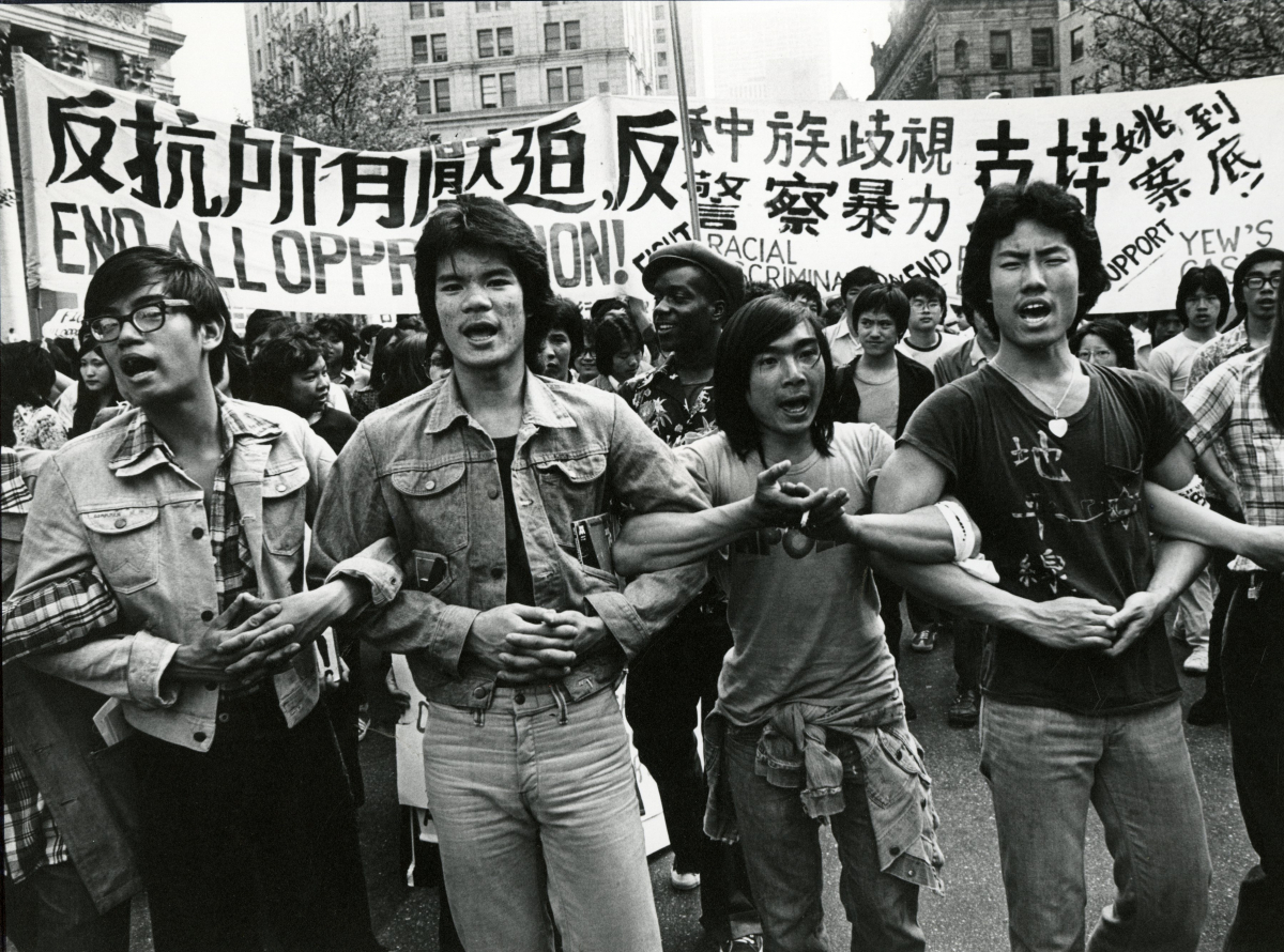 Four Asian American men linking arms in front of banners in Chinese and English.
